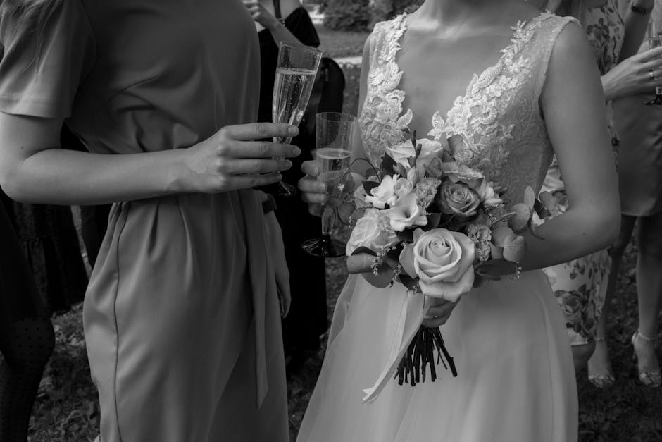 A bride holding a floral bouquet featuring large, pale roses, lisianthus, and greenery, arranged with a mix of pastel and neutral tones. She is dressed in an elegant lace wedding gown with intricate e