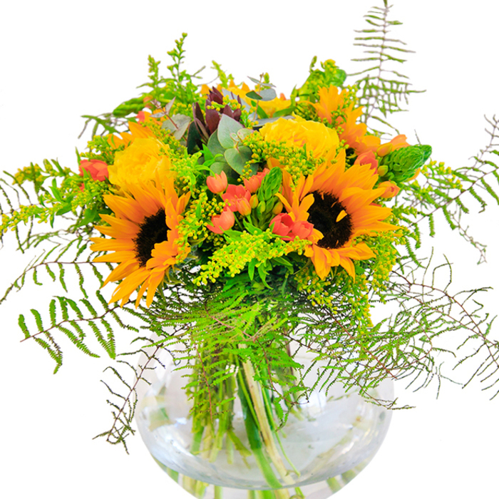This richly textured autumn bouquet radiates the essence of Mill Hill's natural beauty as seen on a late summer afternoon. Grand sunflowers with rich, tawny centers and golden petals form the heart of the display, their cheerful faces open wide as if to greet each visitor to NW7. Surrounding them, tightly coiled yellow garden roses unfurl, emitting a subtle, sweet fragrance reminiscent of country gardens near Arrandene Open Space. Red Hypericum berries, gleaming among the greenery, offer bold contrast and playful charm, much like the bursts of colour in Mill Hill's local markets. Light-green fillers-possibly solidago-dot the composition with airy, star-like blossoms, while slender green spikes and waterfalls of ferns add wild, untamed movement. Soft silvery eucalyptus leaves slip through, imparting a rustic, natural finish. Set within a crystal-clear, spherical vase that lets every fresh stem show, the bouquet is a vision of abundance and artistry. This arrangement, perfect for celebrating milestones or simply infusing a home with Mill Hill joy, weaves together the richness of the season and the skill of a neighborhood florist.